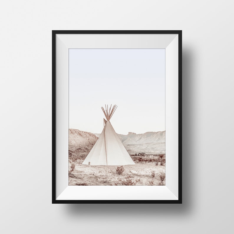 May include: A white teepee tent stands in a desert landscape with brown hills and a light blue sky. The teepee is made of canvas and has a wooden frame.