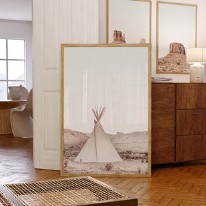 May include: A framed print of a white teepee in a desert landscape. The print is in a light brown wood frame and is hanging on a white wall. There is a wooden dresser with drawers below the print.