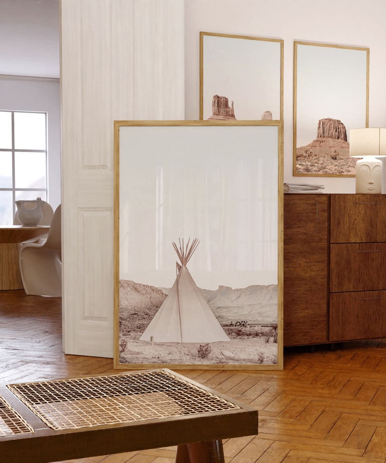 May include: A framed print of a white teepee in a desert landscape. The print is in a light brown wood frame and is hanging on a white wall. There is a wooden dresser with drawers below the print.