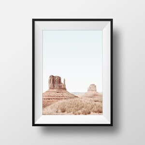 May include: A framed photograph of two red rock formations in a desert landscape. The sky is a pale blue and the ground is covered in dry grass.