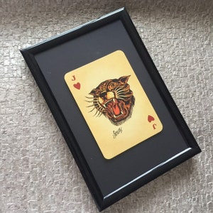 May include: A framed print of a vintage playing card featuring a snarling tiger head with a red heart suit. The card is the Jack of Hearts.