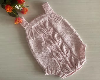 Könnte beinhalten: Ein hellrosa gestrickter Baby-Strampler mit Blattmuster. Der Strampler hat Träger und ein strukturiertes Design. Das Kleidungsstück ist aus weichem Garn gefertigt und für ein Baby geeignet.