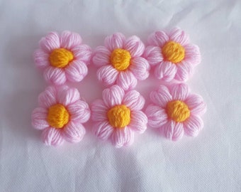 May include: Six pink crocheted flowers with yellow centers. The flowers are arranged in two rows of three.