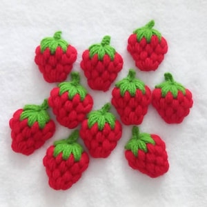Può includere: Dieci fragole all'uncinetto rosse e verdi. Le fragole sono fatte di filato e hanno una superficie testurizzata.