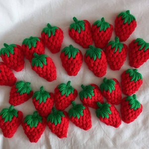 May include: A selection of red crocheted strawberries with green leafy tops. The handmade berries are arranged on a white surface, highlighting the vibrant red colour and detailed stitching. These decorative items are suitable for crafting or home decor.