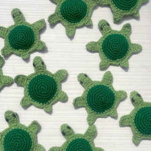 Pode incluir: Apliques de tartaruga de crochê feitos à mão em tons de verde. Cada tartaruga apresenta uma carapaça verde escura e um corpo verde mais claro com barbatanas e cabeça. Ideais para projetos de artesanato.
