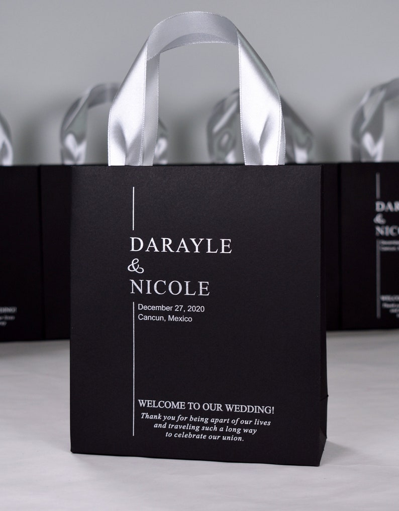 K&ouml;nnte beinhalten: Schwarze und wei&szlig;e Hochzeitstasche mit einem silbernen Schleifenhenkel. Die Tasche tr&auml;gt die Namen "Darayle & Nicole" und das Datum "27. Dezember 2020". Die Tasche tr&auml;gt auch den Text "Willkommen zu unserer Hochzeit! Vielen Dank, dass Sie Teil unseres Lebens sind und so weit gereist sind, um unsere Vereinigung zu feiern."