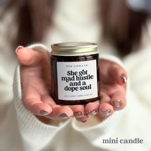 May include: A brown glass candle with a gold lid and white label. The label reads 'WINK CANDLE CO. She got mad hustle and a dope soul 4OZ SWEET BERRY VANILLA'.