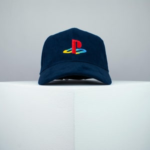 May include: A navy blue baseball cap with a red, yellow, blue, and white PlayStation logo embroidered on the front.