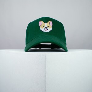 May include: A green baseball cap with an embroidered image of a smiling corgi.