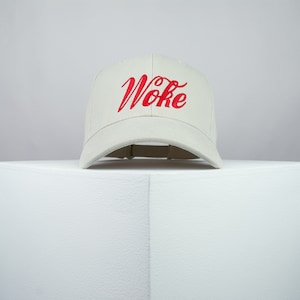 Op de afbeelding: Een witte baseballpet met een rood geborduurd "Woke" op de voorkant.