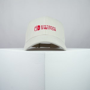 May include: A white baseball cap with a red Nintendo Switch logo embroidered on the front.