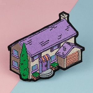 Könnte beinhalten: Gestickter Bügel-Patch einer Cartoon-Haus mit einem violetten Dach, braunen Wänden und einem grünen Baum im Vorgarten. Das Haus hat eine Garagentür, eine Haustür und Fenster.