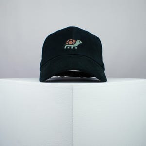 May include: A black baseball cap with a small embroidered turtle design on the front.