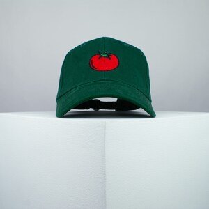 May include: A green baseball cap with a red tomato embroidered on the front.