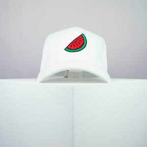 Puede incluir: Gorra de béisbol blanca con una rodaja de sandía roja y verde bordada en la parte delantera.