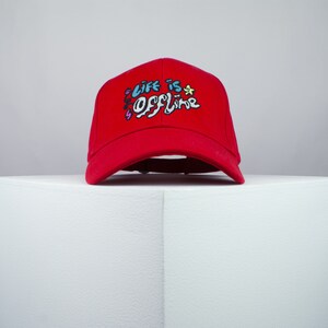 May include: Red baseball cap with the text "Life is Offline" embroidered in colorful lettering.