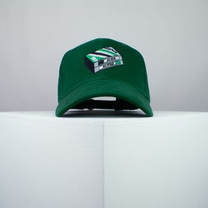 May include: A green baseball cap featuring an embroidered image of a VHS tape labelled "Alien" and "Aliens".