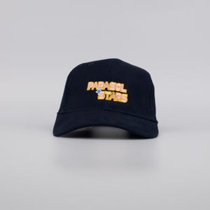 May include: A navy blue baseball cap with the text "PARASOL STARS" in yellow and blue. The cap has a curved brim and a structured crown. The hat is made of a durable fabric.