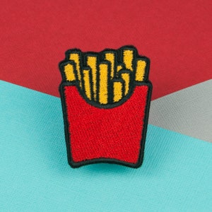 以下が含まれることがあります： フライドポテトの箱の刺繍パッチ。フライドポテトは黄色で、箱は黒のアウトラインで赤です。