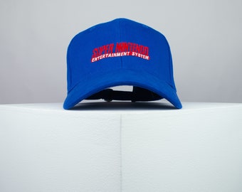 May include: A royal blue baseball cap with red embroidered text that reads "SUPER NINTENDO ENTERTAINMENT SYSTEM".