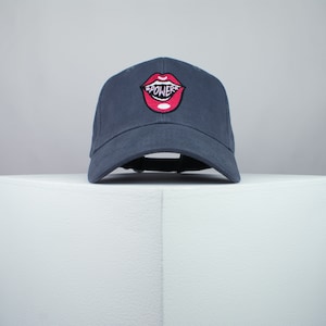 May include: A dark blue baseball cap with a red embroidered mouth with the word "POWER" inside.