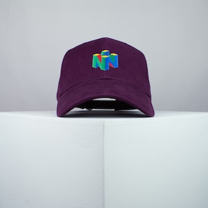 May include: A purple baseball cap with an embroidered Nintendo 64 logo in yellow, blue, green, and red.