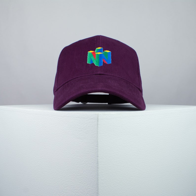 May include: A purple baseball cap with an embroidered Nintendo 64 logo in yellow, blue, green, and red.