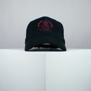 Op de afbeelding: Zwarte baseballcap met de roze geborduurde tekst "MISTER STRONG". De cap heeft een gebogen klep en een ontwerp met zes panelen. De afbeelding is een gestileerde illustratie van een gespierde figuur.