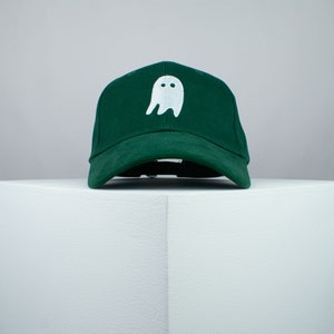 Puede incluir: Una gorra de béisbol verde oscuro con un fantasma blanco bordado en la parte delantera.