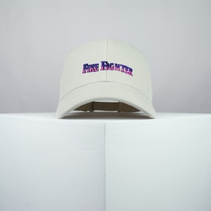 May include: A white baseball cap with a pink and purple "FIRE FIGHTER" embroidered on the front.