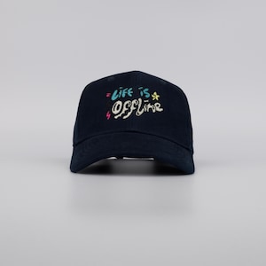 May include: A navy blue baseball cap with the text "= life is offline" in colorful, handwritten-style lettering. The cap has a curved brim and a structured crown, suitable for casual wear.