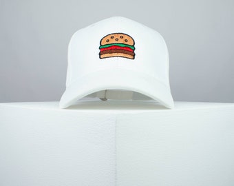 May include: White baseball cap with an embroidered image of a hamburger on the front.
