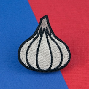 May include: A white embroidered garlic clove patch with black stitching, on a blue and red background.
