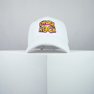 May include: White baseball cap with a pink and yellow embroidered logo that says "Chuck Rock"