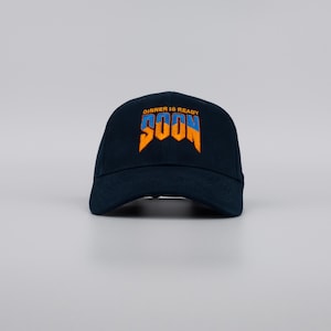 Può includere: Cappellino da baseball blu navy con la scritta ricamata "DINNER IS READY SOON" in arancione e blu. Il cappellino ha una visiera curva e un classico design a sei pannelli, adatto per un abbigliamento casual.