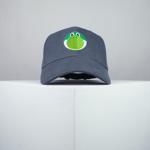 May include: A dark grey baseball cap with a green and white embroidered character on the front.