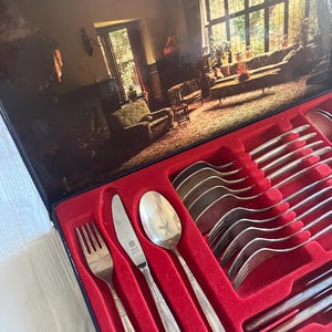 May include: A set of silver cutlery in a red velvet lined box. The cutlery includes forks, knives, and spoons. The box is open and the cutlery is arranged in rows.