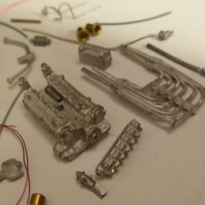 Könnte beinhalten: Eine Sammlung kleiner, silberfarbener Metall-Modellmotorteile, darunter ein Motorblock, Auspuffkrümmer und verschiedene andere Komponenten. Einige Teile sind verstreut, mit Drähten und Messingarmaturen sichtbar.