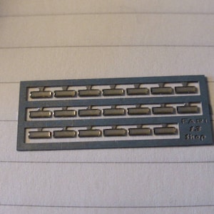 Könnte beinhalten: Eine graue Plastikfolie mit 24 rechteckigen silberfarbenen Formen, die in drei Reihen zu acht angeordnet sind. Die Folie trägt den Aufdruck "FARI 1/3 Shop" auf der rechten Seite.