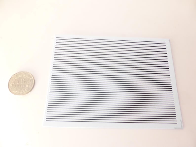 Puede incluir: Una tarjeta rectangular blanca con l&iacute;neas negras paralelas espaciadas uniformemente. A la izquierda de la tarjeta hay una moneda plateada con caracteres japoneses. El fondo es de color rosa claro.