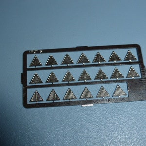 May include: A sheet of metal with 21 silver-coloured triangle shapes, each with a textured surface. The triangles are arranged in three rows of seven. The sheet is labelled "P.M.G."