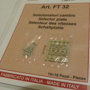 May include: A close-up of a plastic bag containing a sheet of metal parts and small metal screws. The bag is labelled "Art. FT 32" and includes the text "Selezionatori cambio, Selector plate, Sélecteur des vitesses, Schaltplatte, 16+16 Pezzi - Pieces, FABBRICATO IN ITALIA - MADE IN ITALY".