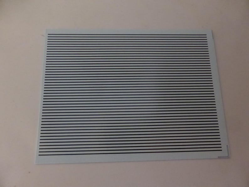 Puede incluir: Una hoja rectangular con un fondo azul claro y l&iacute;neas horizontales negras espaciadas uniformemente. Las l&iacute;neas crean un patr&oacute;n de rayas. La hoja se coloca sobre un fondo liso blanquecino. Las l&iacute;neas son paralelas.