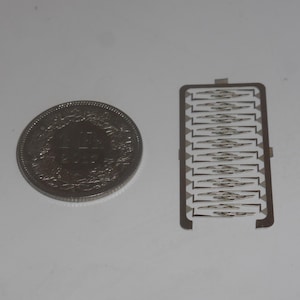 May include: A silver coin with a design featuring a cross and the text "1/2 FRANC 1938" and a silver sheet of metal with a pattern of small, thin, rectangular shapes.