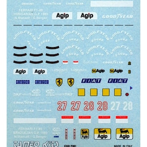 Puede incluir: Una hoja de calcomanías Ferrari F1-89 con varios logotipos, texto y números. Incluye "Agip", "Goodyear", "Fiat" y nombres de pilotos. Presenta los números 27 y 28 en rojo. Fabricado en Italia.