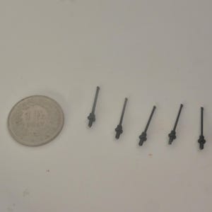 May include: A collection of small, dark gray metal objects resembling miniature swords, arranged near a silver coin. The coin has text and a date. The objects have a handle-like base and a thin, elongated blade.