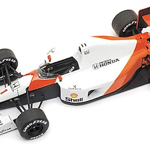 May include: A white, orange, and black Formula 1 race car model. The car features sponsor logos including Shell, Honda, and Goodyear. The tires are black with white lettering. The car has the number 1 on the side.