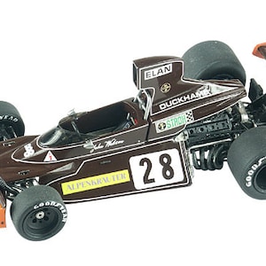 May include: A brown and orange vintage race car model, featuring the number 28. The model has sponsor logos such as "ELAN", "DUCKHAMS", and "GOOD YEAR" tyres. The rear wing displays "JOHN GOLDIE RACING WITH RADIO LUXEMBOURG".