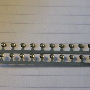 May include: A silver strip with 2 rows of 16 small, round, metallic, dome-shaped buttons with a clear, slightly yellowed center.